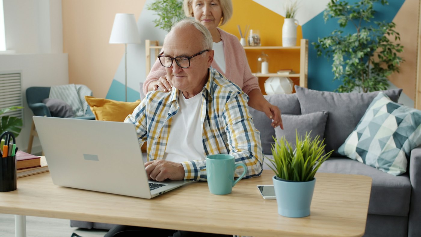 Un couple de retraités souriants devant un ordinateur portable